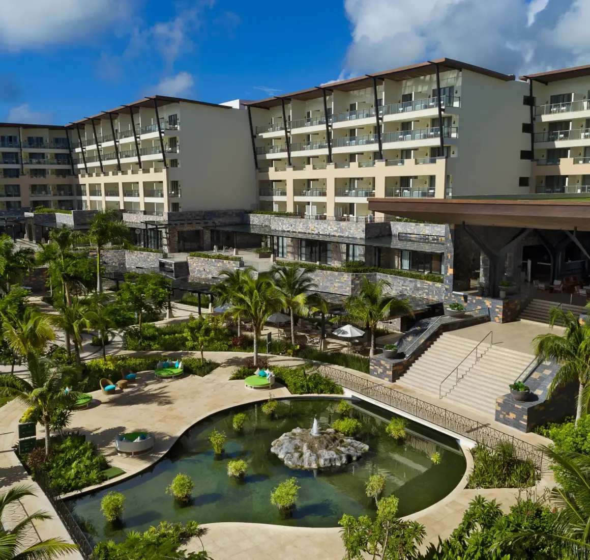Resort garden area with tropical landscaping, a central fishpond, and surrounding lush palm trees.
