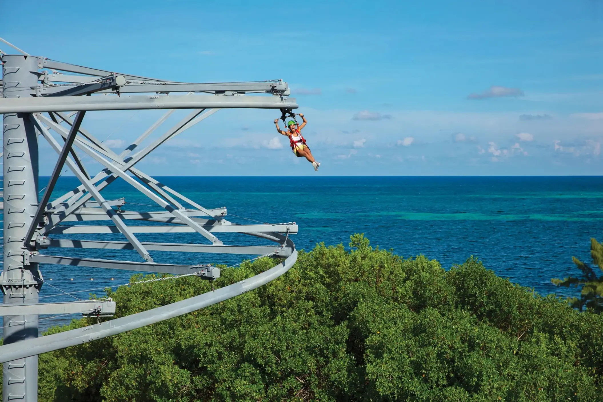 Guest riding a rollglider zipline over lush greenery with panoramic views of the Caribbean Sea.