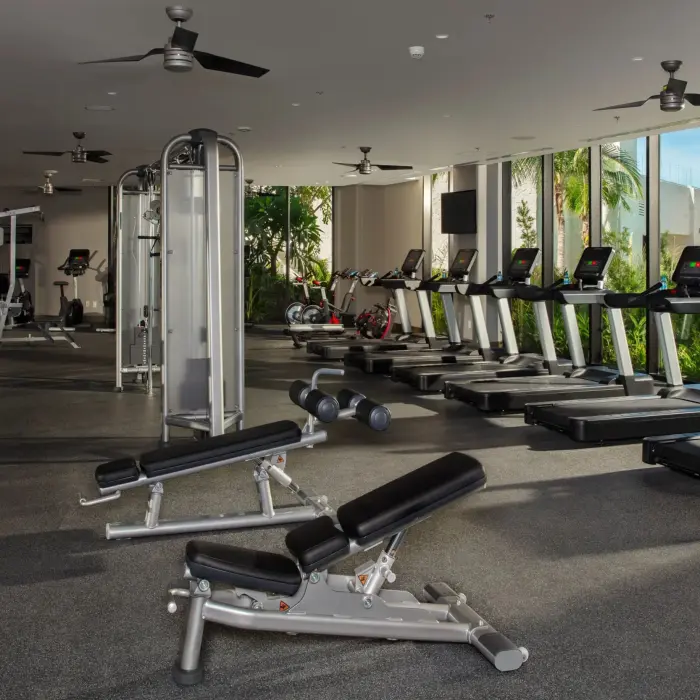Spacious resort gym with treadmills, weight machines, and garden views through glass walls.