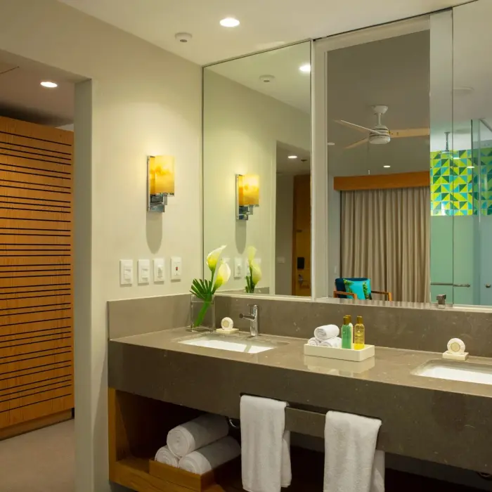 Elegant bathroom with twin sinks, large mirror and modern lighting, reflecting cozy interior with tropical details.