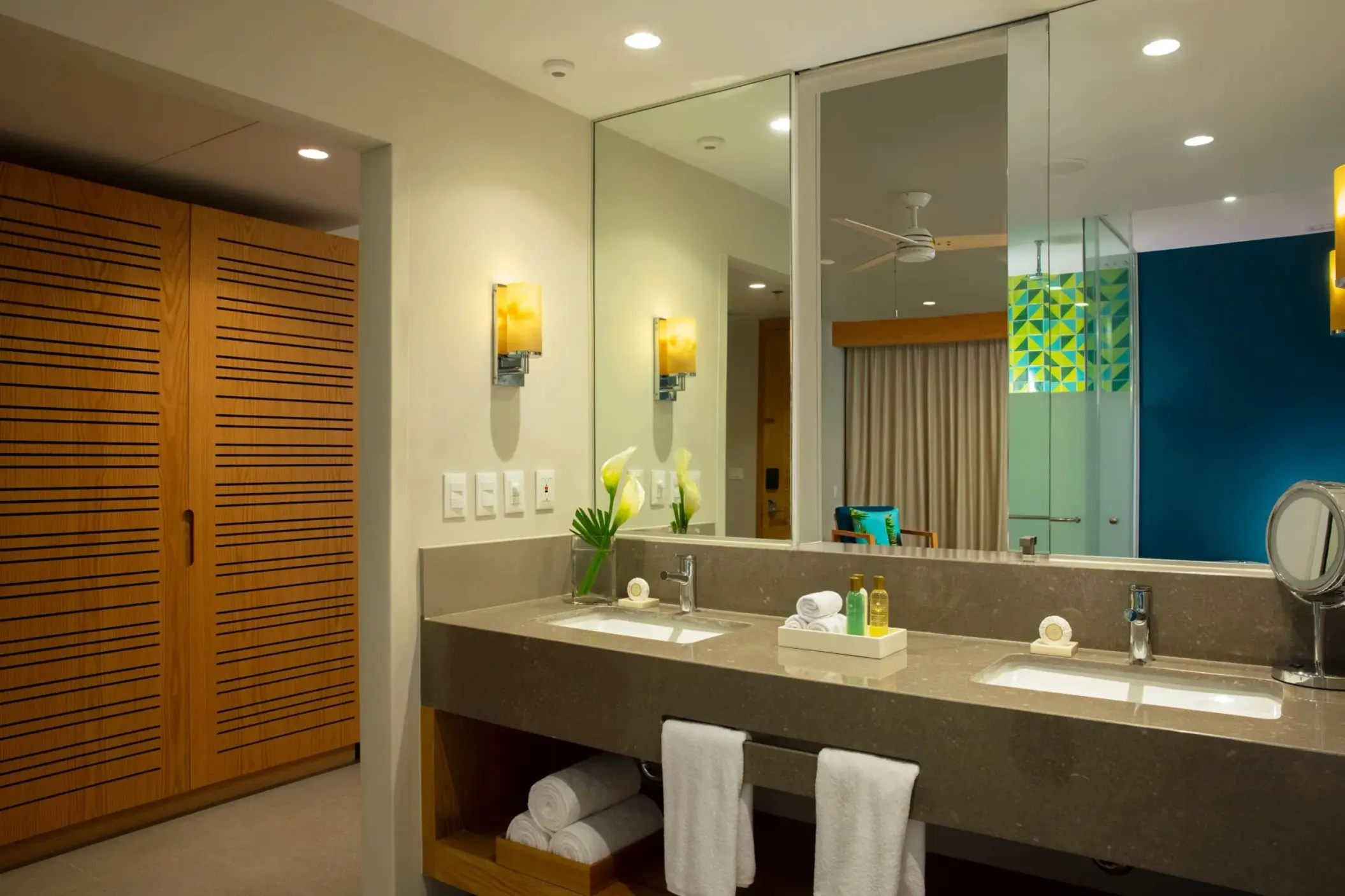 Elegant bathroom with twin sinks, large mirror and modern lighting, reflecting cozy interior with tropical details.