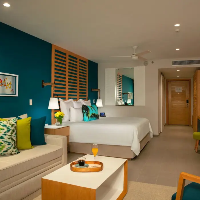 Colorful junior suite with king bed, deep teal accent wall, and cozy sitting area with vibrant pillows.