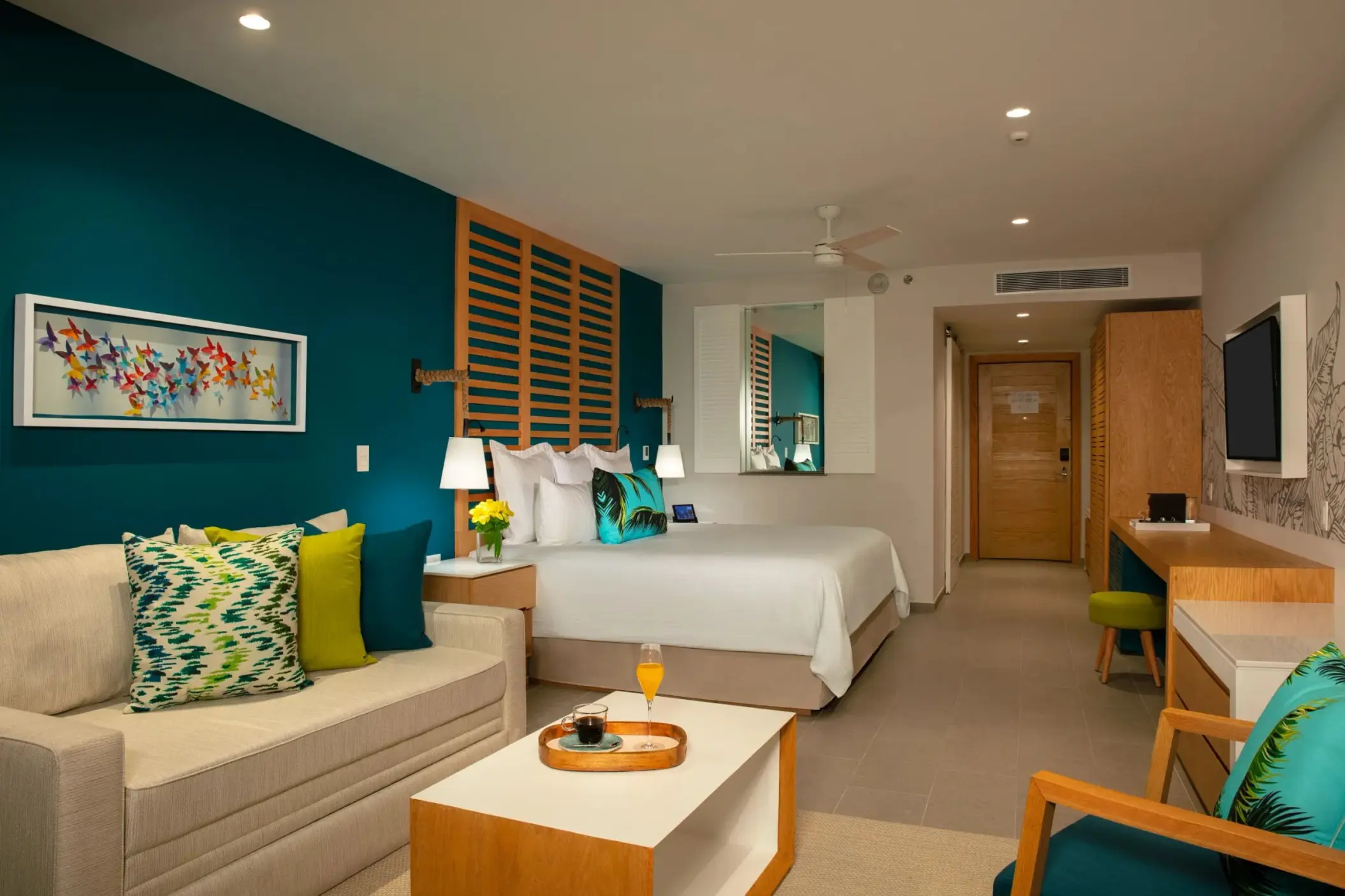 Colorful junior suite with king bed, deep teal accent wall, and cozy sitting area with vibrant pillows.