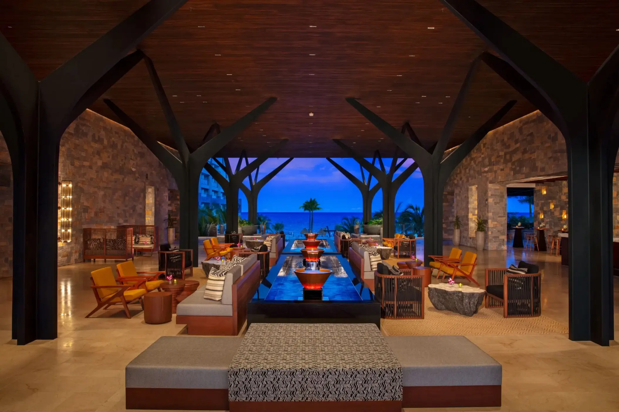 Sophisticated open-air resort lobby with lounge seating, modern design, and a view of the ocean at dusk.