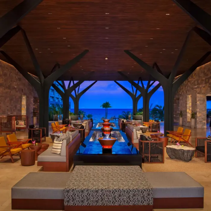 Sophisticated open-air resort lobby with lounge seating, modern design, and a view of the ocean at dusk.