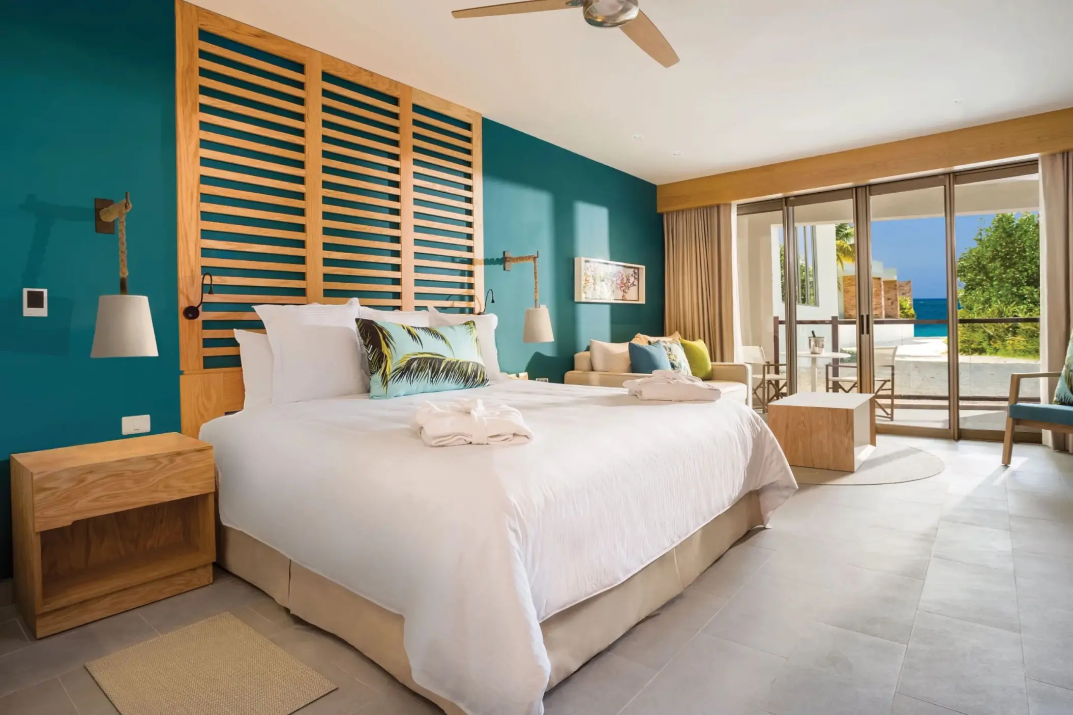 Stylish junior suite with king bed, teal accent wall, and patio view of garden and ocean beyond.