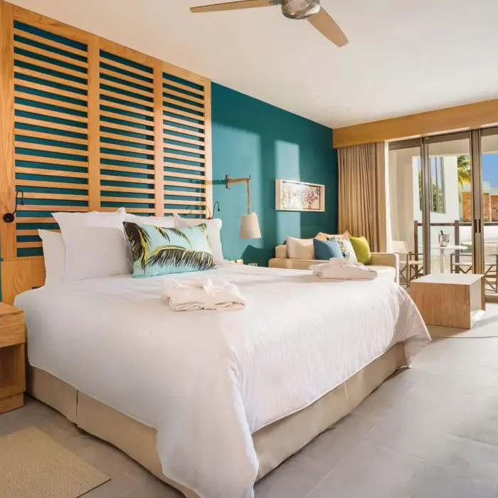 Stylish junior suite with king bed, teal accent wall, and patio view of garden and ocean beyond.