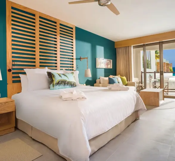 Stylish junior suite with king bed, teal accent wall, and patio view of garden and ocean beyond.