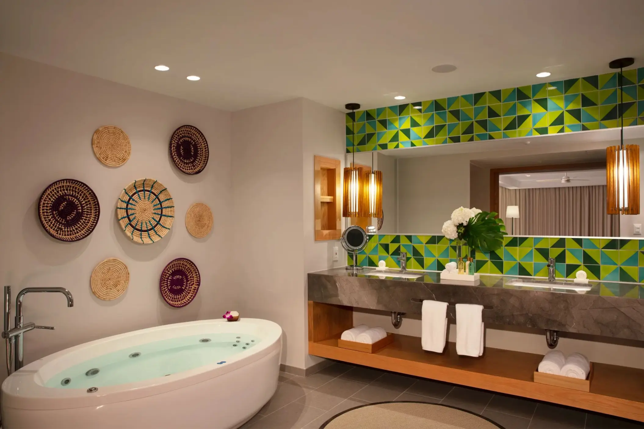 Chic master bathroom with soaking tub, dual sinks, decorative woven wall plates, and bold green tile backsplash.
