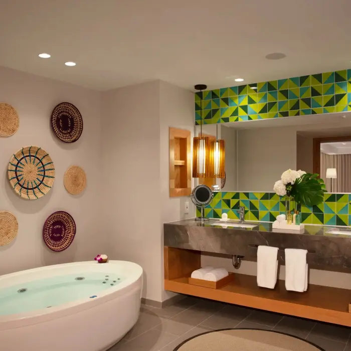 Chic master bathroom with soaking tub, dual sinks, decorative woven wall plates, and bold green tile backsplash.