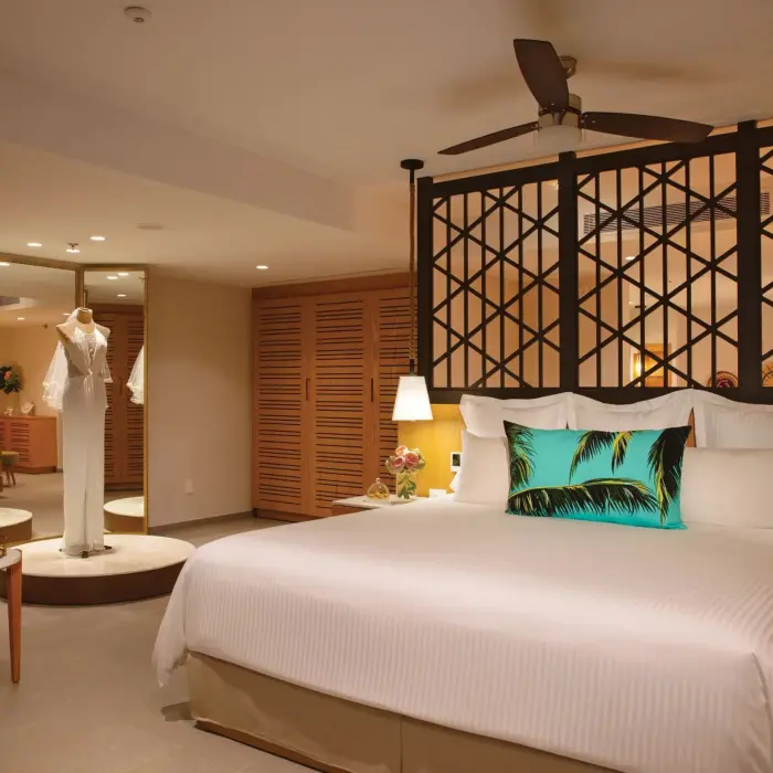 Elegant suite with a king bed, tropical accent pillow, and a bridal mannequin displayed near a full mirror.