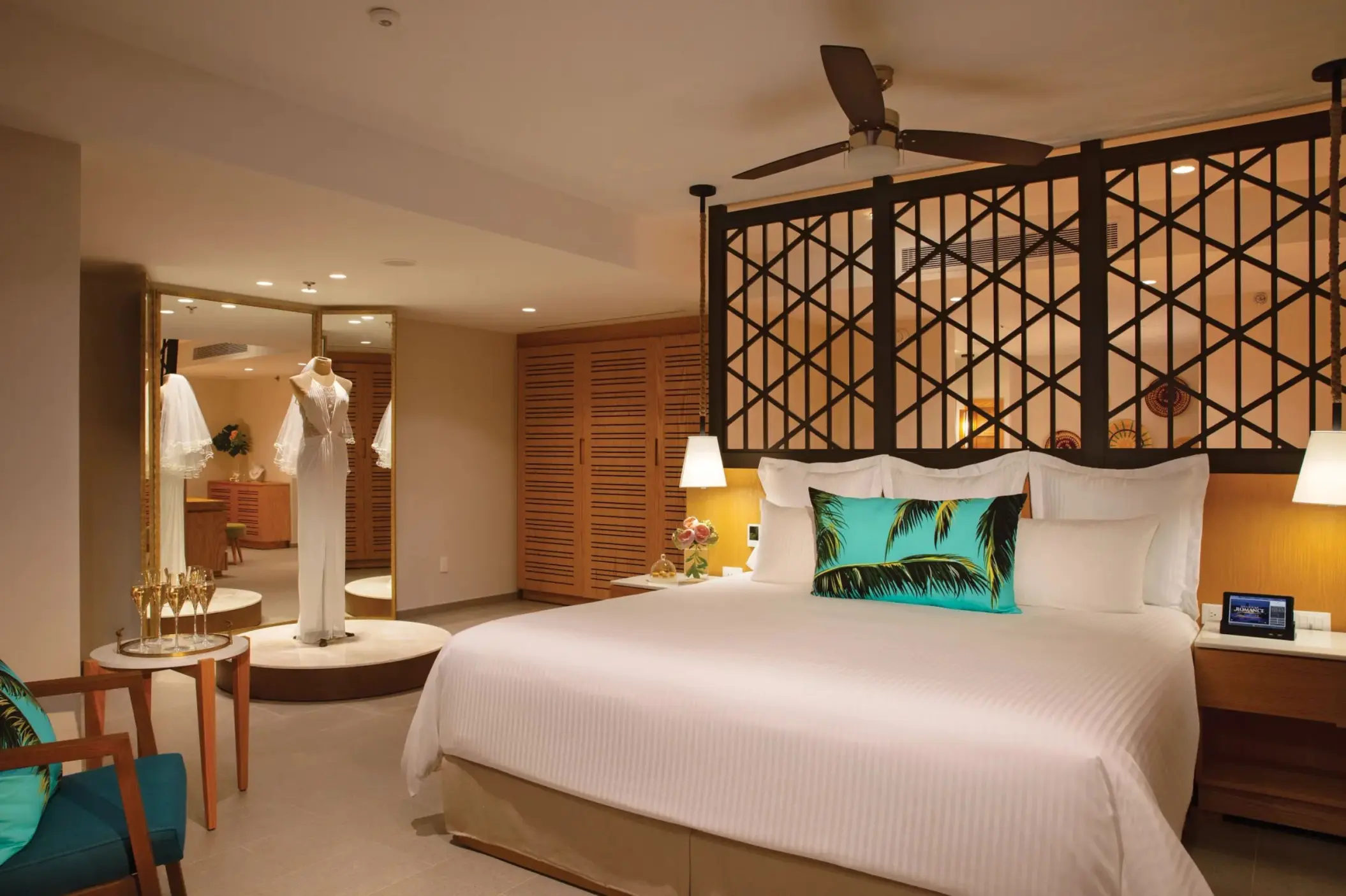 Elegant suite with a king bed, tropical accent pillow, and a bridal mannequin displayed near a full mirror.