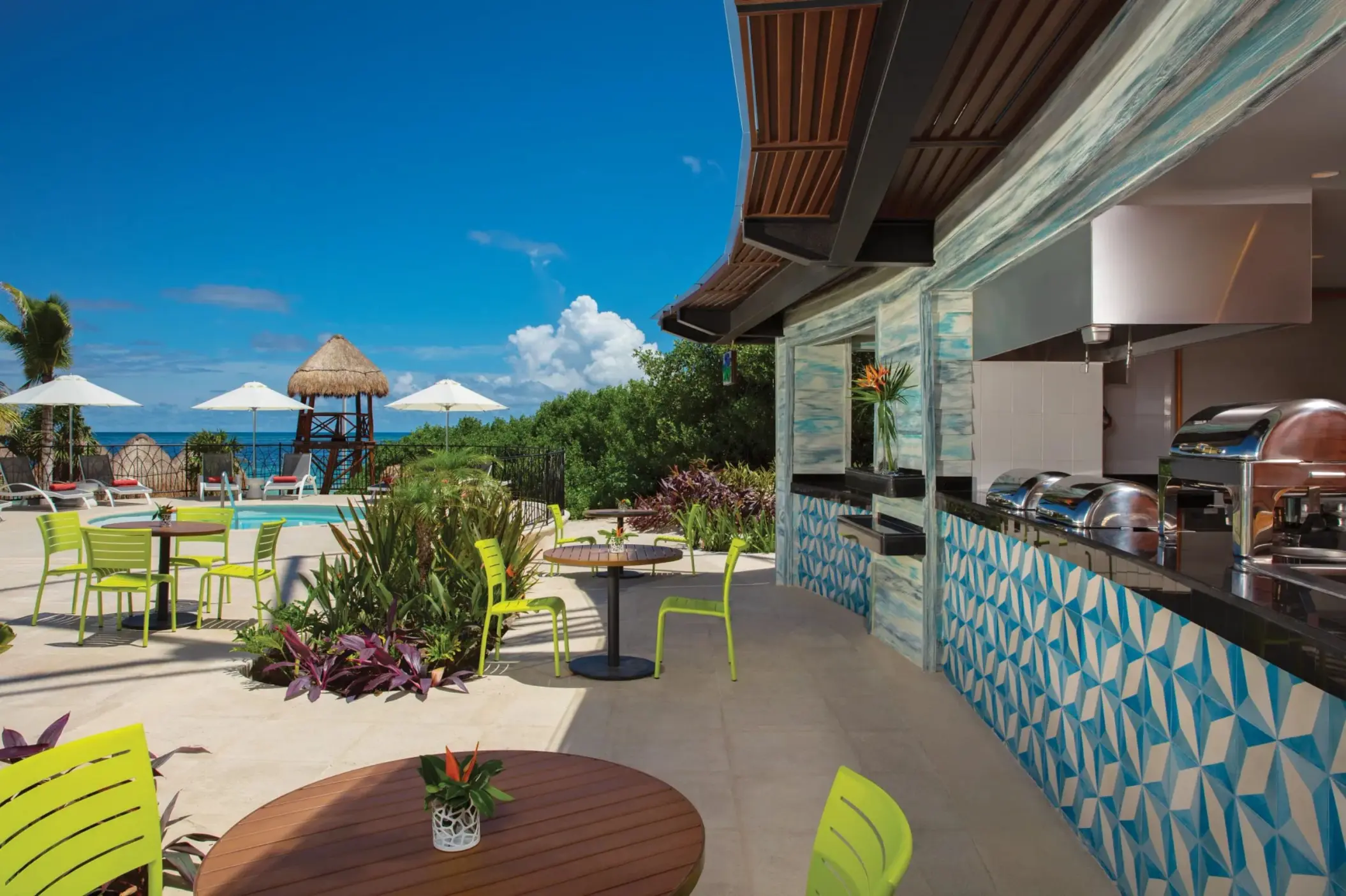 Outdoor grill and dining area with ocean view, tropical plants, and bright seating.
