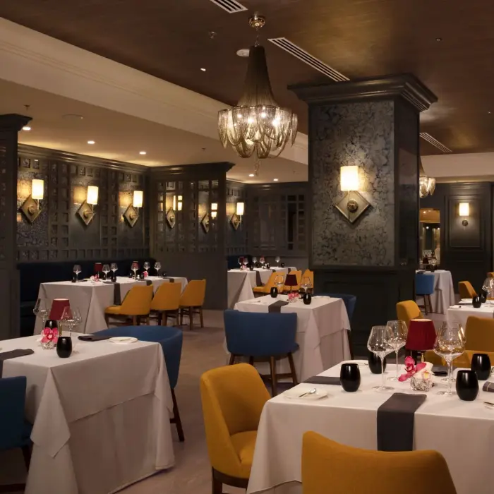 Elegant French dining room with chandelier lighting, colorful chairs, and tables set for fine dining.