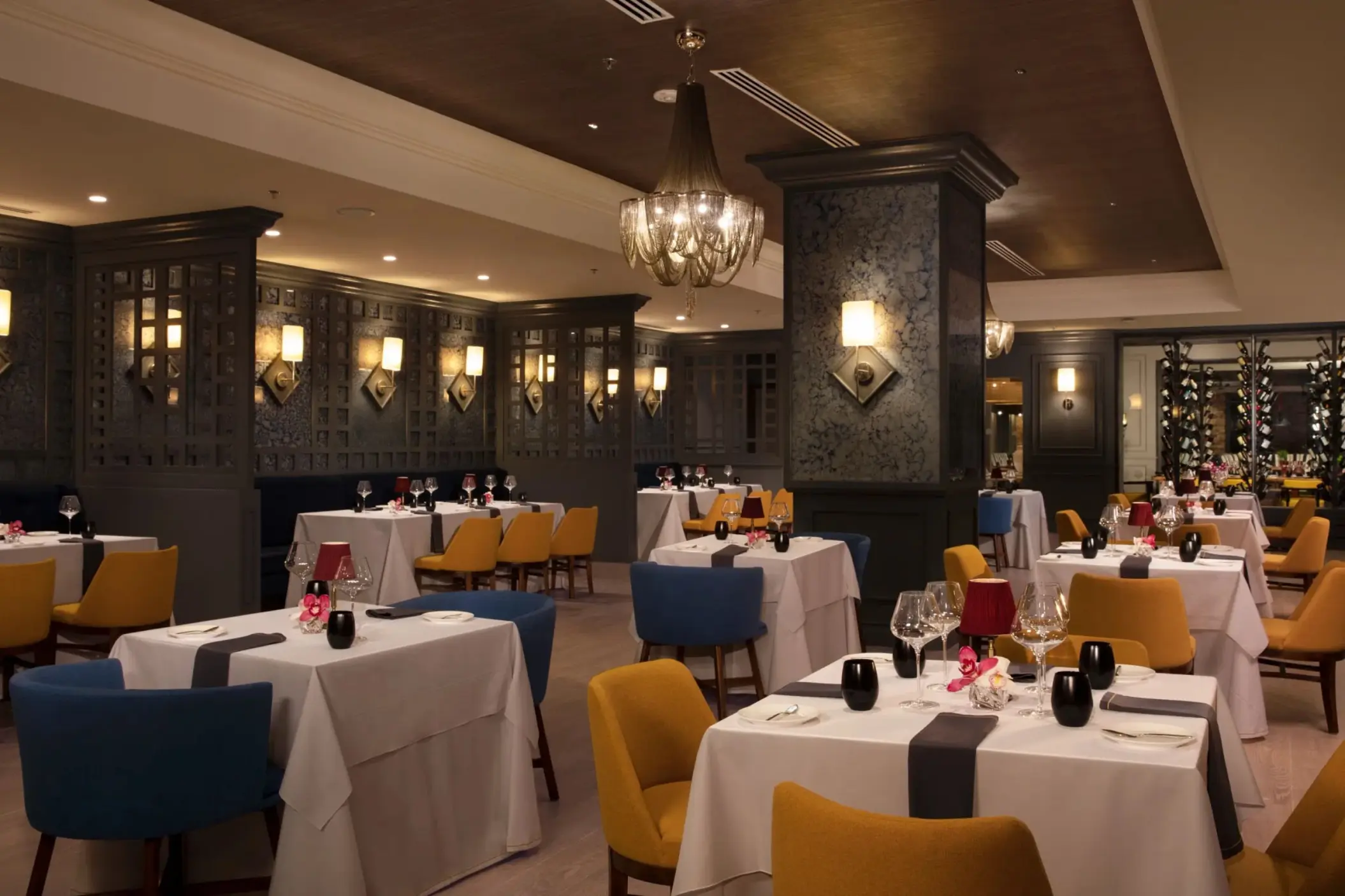 Elegant French dining room with chandelier lighting, colorful chairs, and tables set for fine dining.