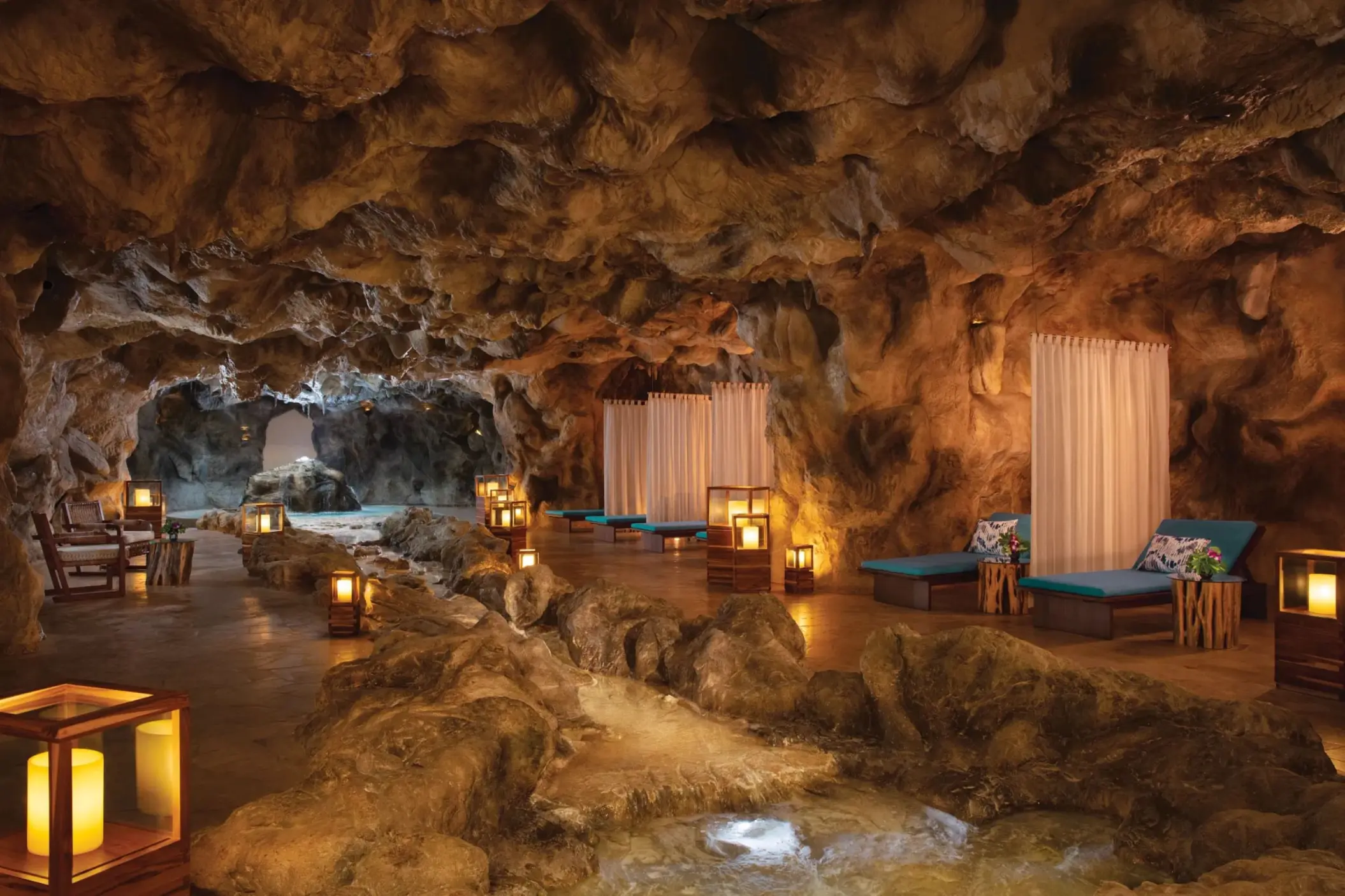 Serene cave pool area with daybeds, flowing water, and warm ambient lantern lighting.