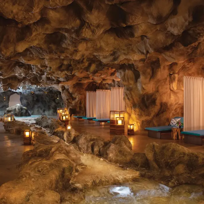 Serene cave pool area with daybeds, flowing water, and warm ambient lantern lighting.