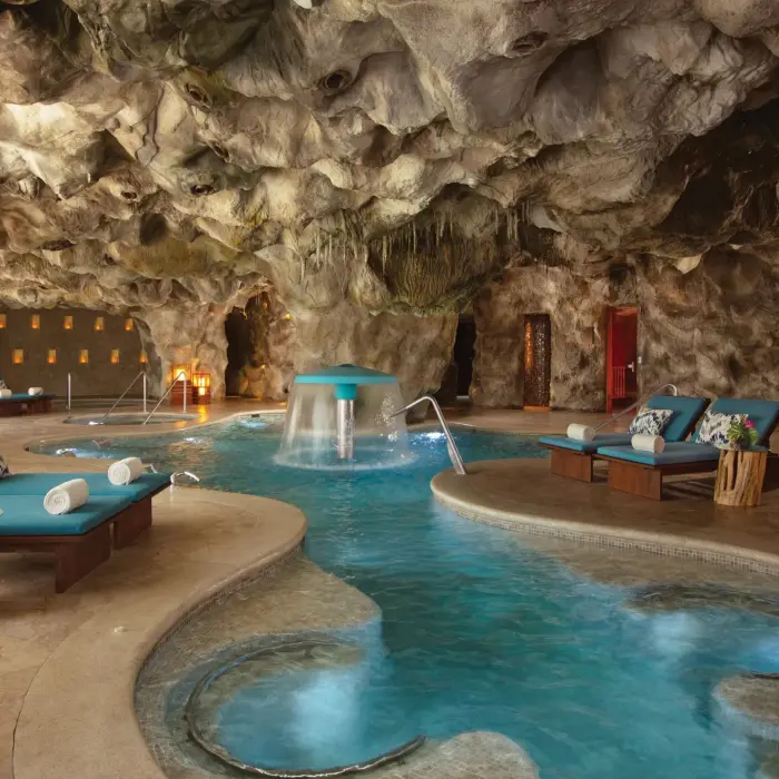 Luxurious indoor hydrotherapy spa pool set in a natural cave-like setting with loungers and ambient lighting.