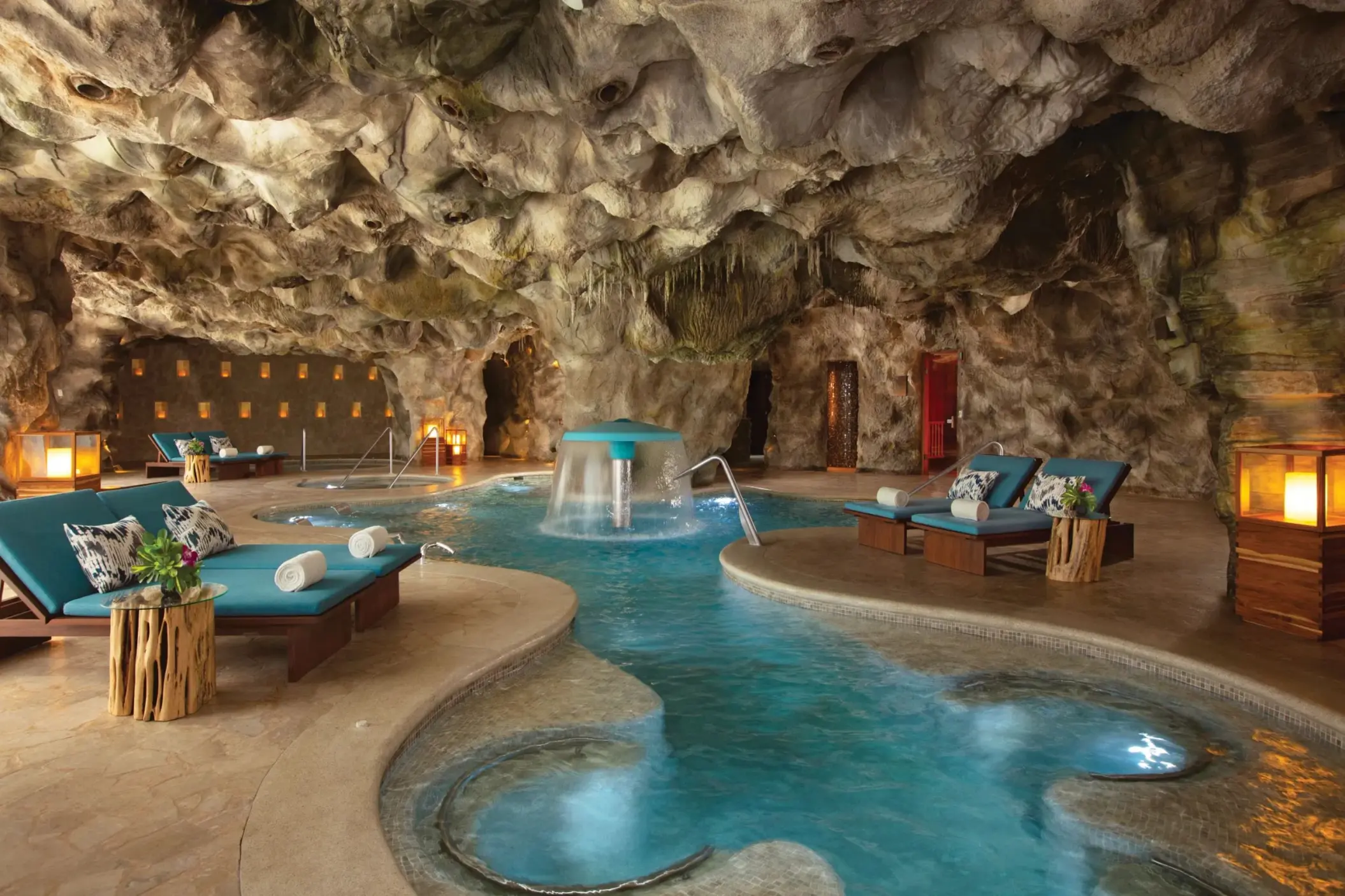 Luxurious indoor hydrotherapy spa pool set in a natural cave-like setting with loungers and ambient lighting.