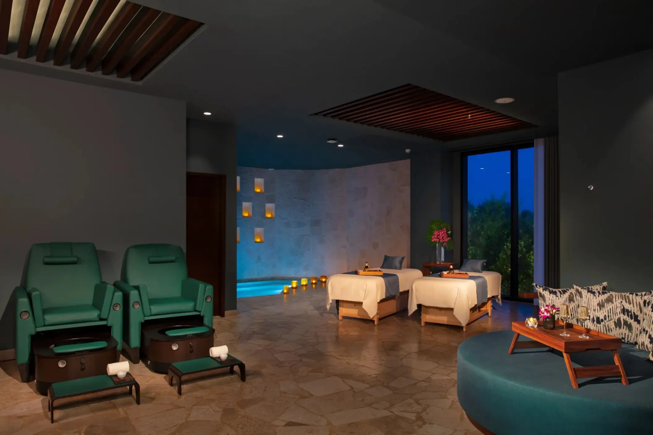 Spa treatment room with massage tables, cozy seating, and ambient lighting.