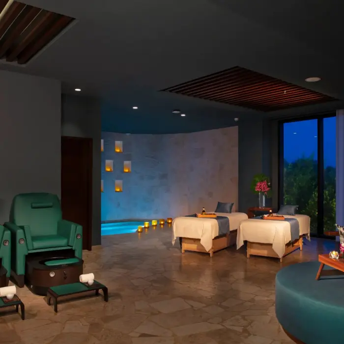 Spa treatment room with massage tables, cozy seating, and ambient lighting.