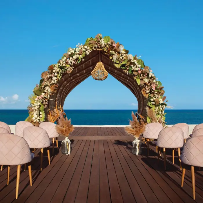 Oceanfront wedding gazebo with floral arch and blush seating, set on a wooden deck under a clear blue sky.