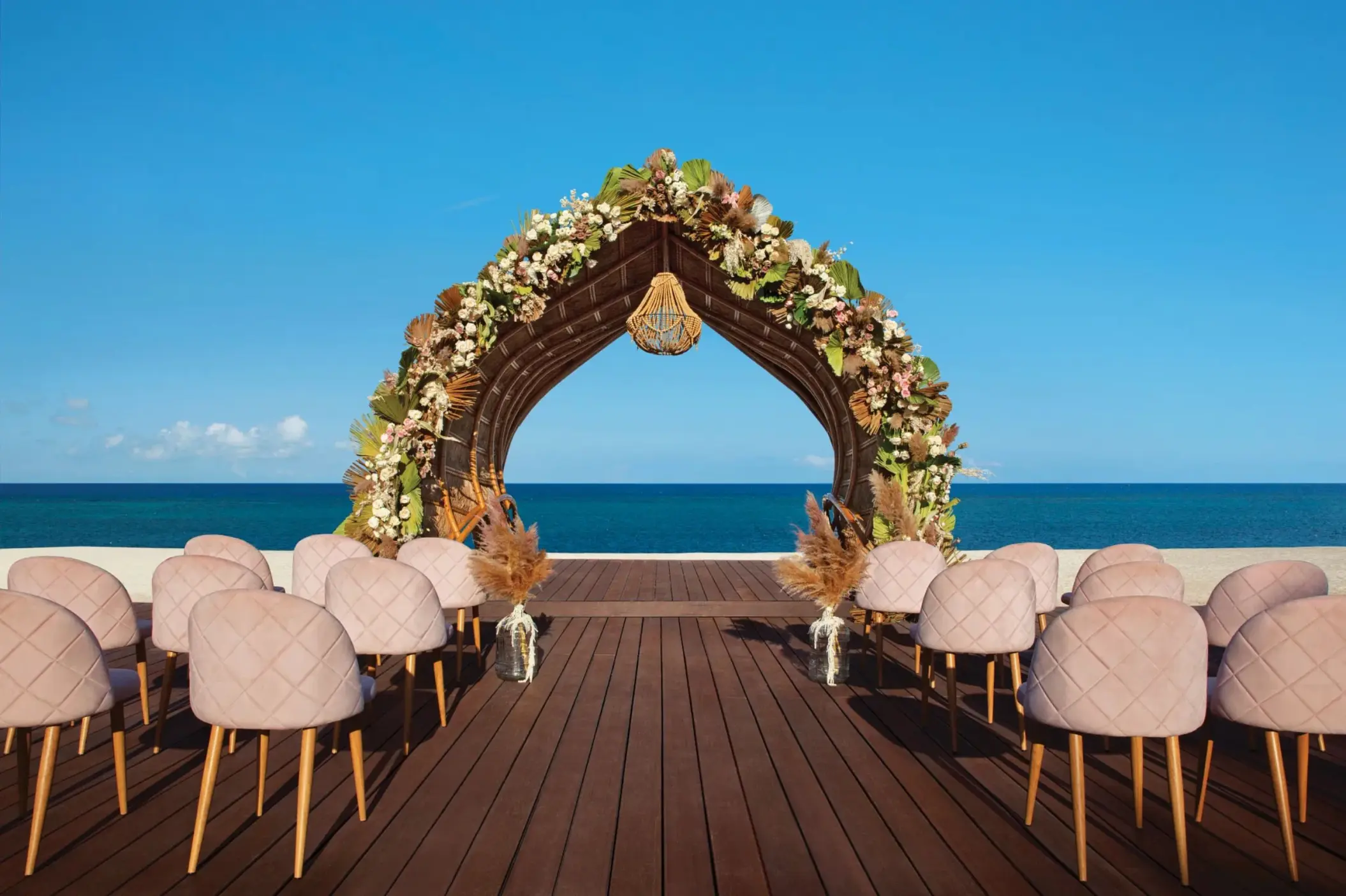 Oceanfront wedding gazebo with floral arch and blush seating, set on a wooden deck under a clear blue sky.