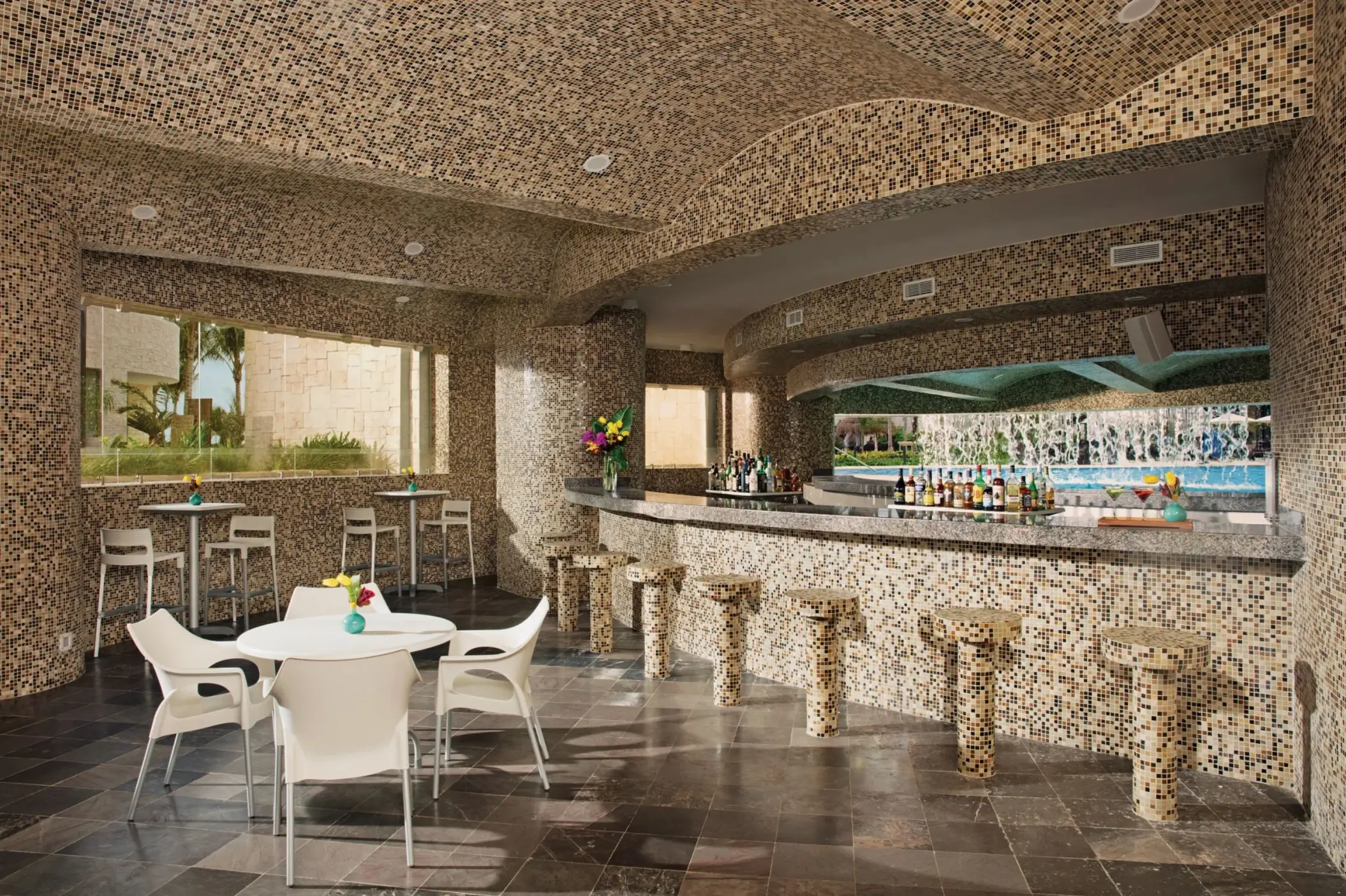 Grotto’s Bar indoor section with mosaic tile design, bar seating, and a view of the pool and garden.