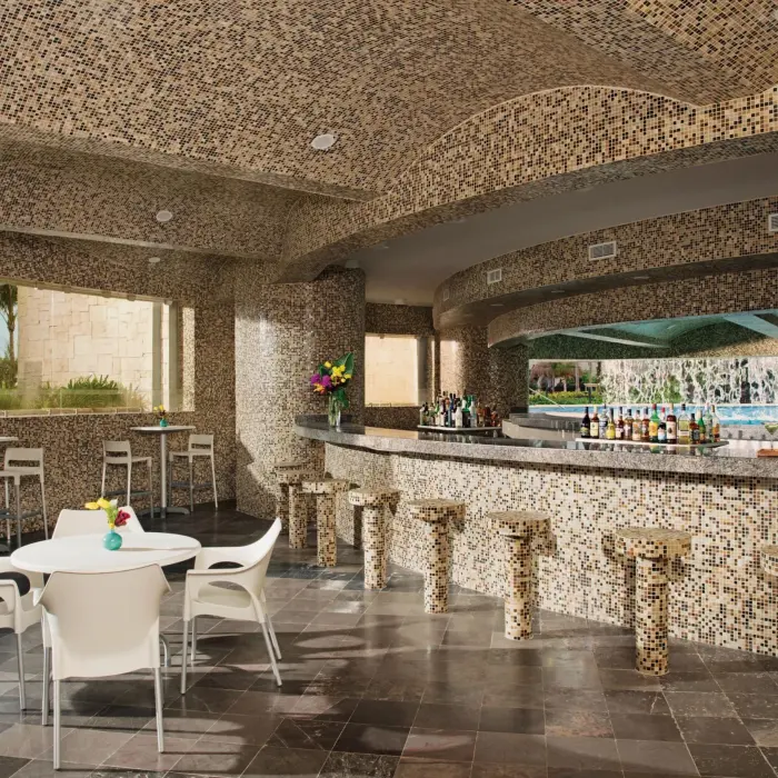 Grotto’s Bar indoor section with mosaic tile design, bar seating, and a view of the pool and garden.