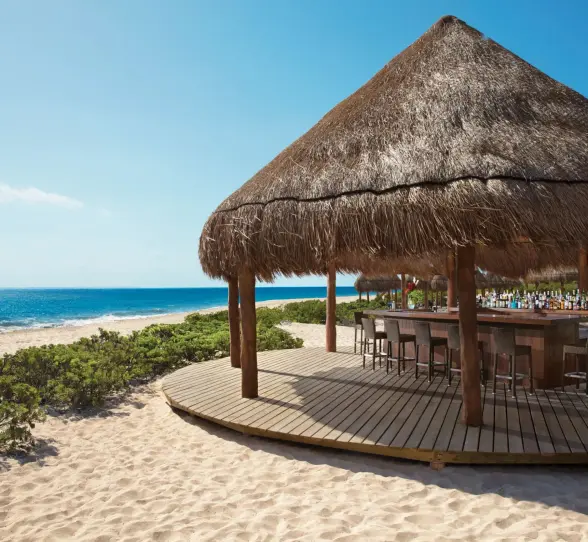 Hideaway Beach Bar under a thatched palapa on the beach, offering direct ocean views and bar seating.