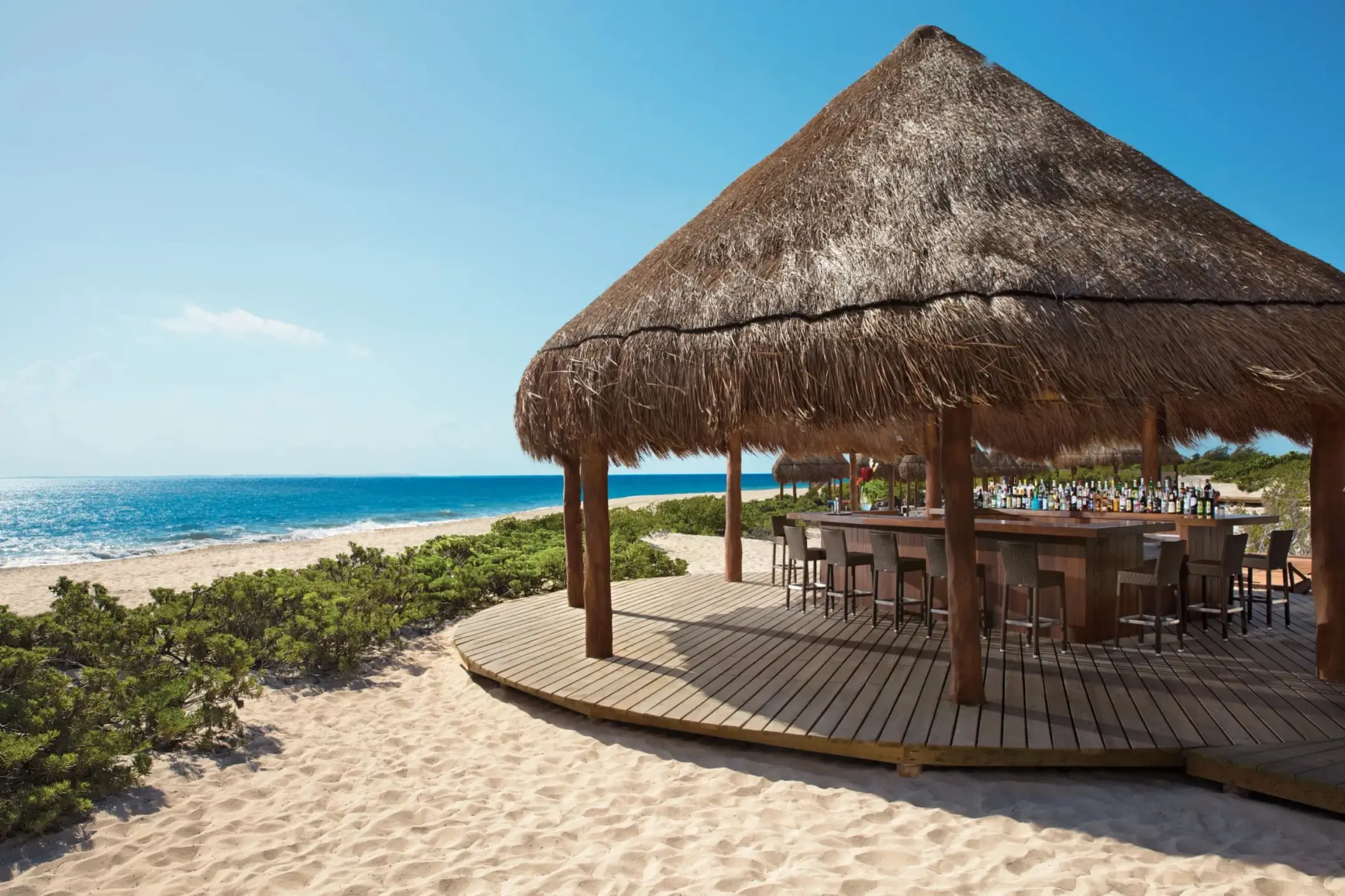 Hideaway Beach Bar under a thatched palapa on the beach, offering direct ocean views and bar seating.