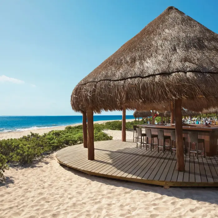 Hideaway Beach Bar under a thatched palapa on the beach, offering direct ocean views and bar seating.