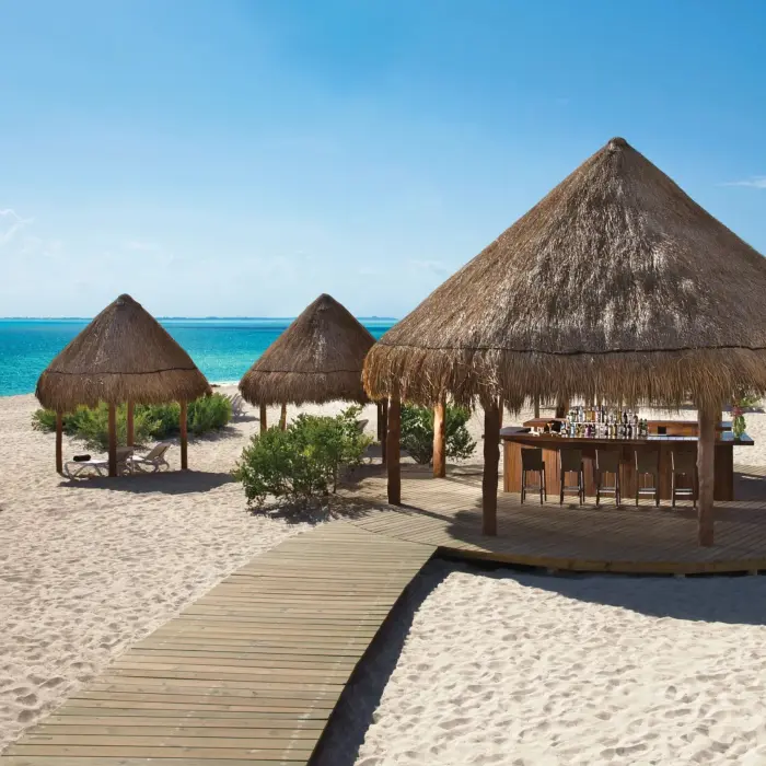 Sandbar beachfront palapa-style bar with wood deck, surrounded by palapas and lounge chairs.