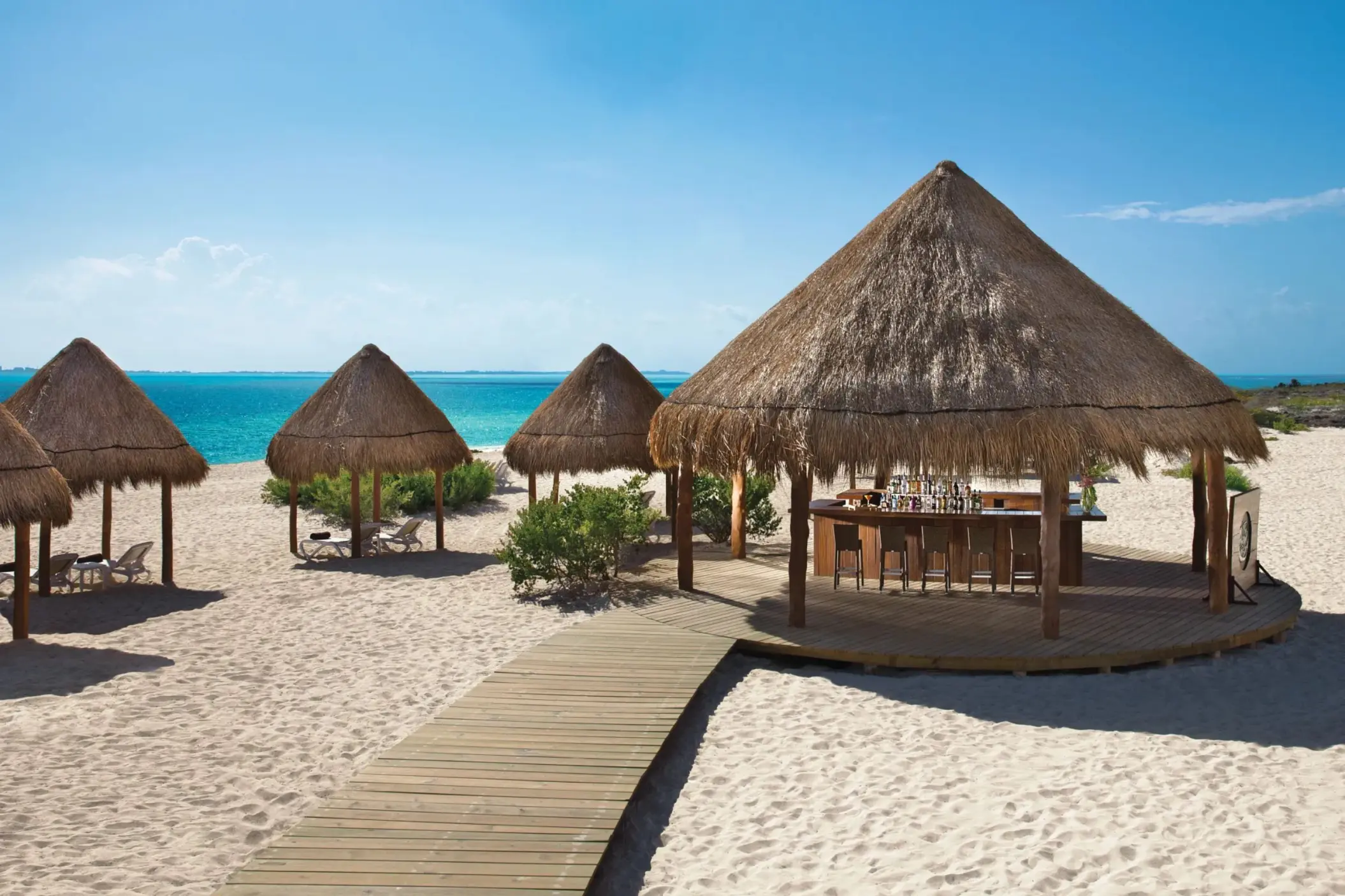 Sandbar beachfront palapa-style bar with wood deck, surrounded by palapas and lounge chairs.