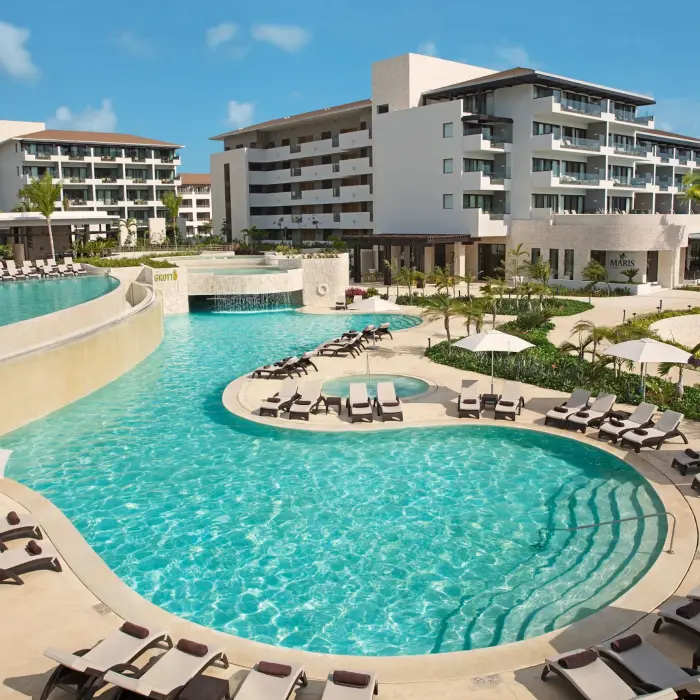 Multi-level pool at Dreams Playa Mujeres with waterfalls, sun loungers, and tropical garden views.