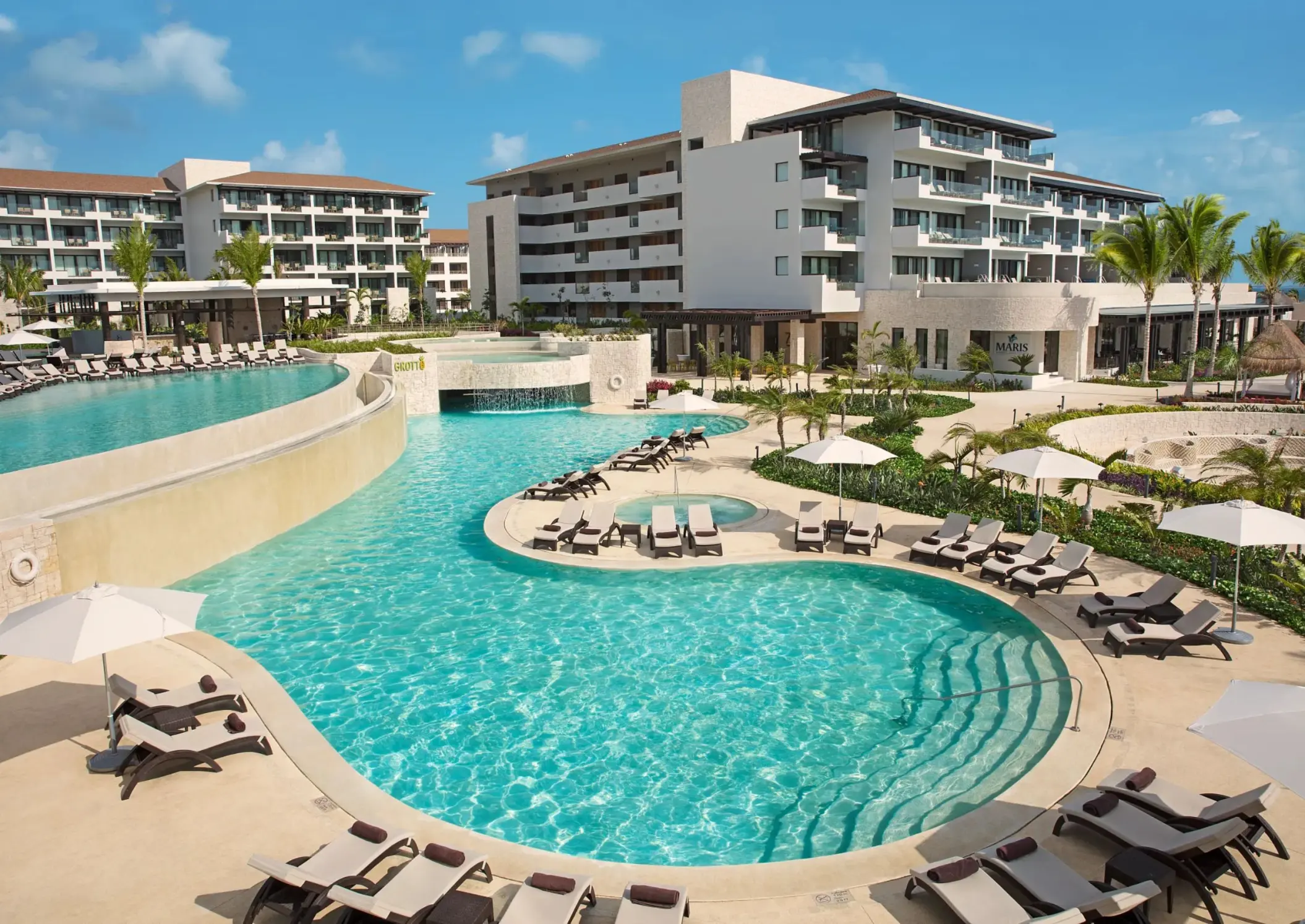Multi-level pool at Dreams Playa Mujeres with waterfalls, sun loungers, and tropical garden views.