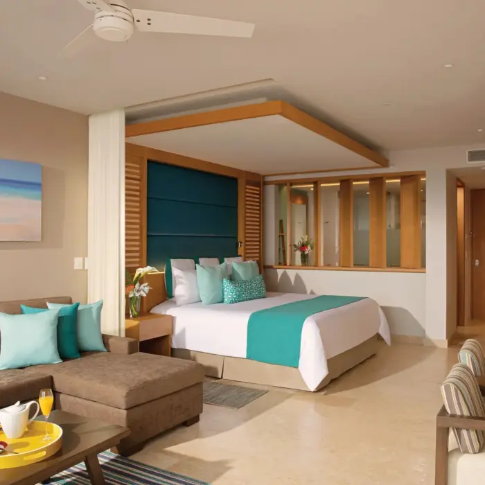 Bright junior suite with teal accents, plush couch, dining space, and a cozy king-size bed.