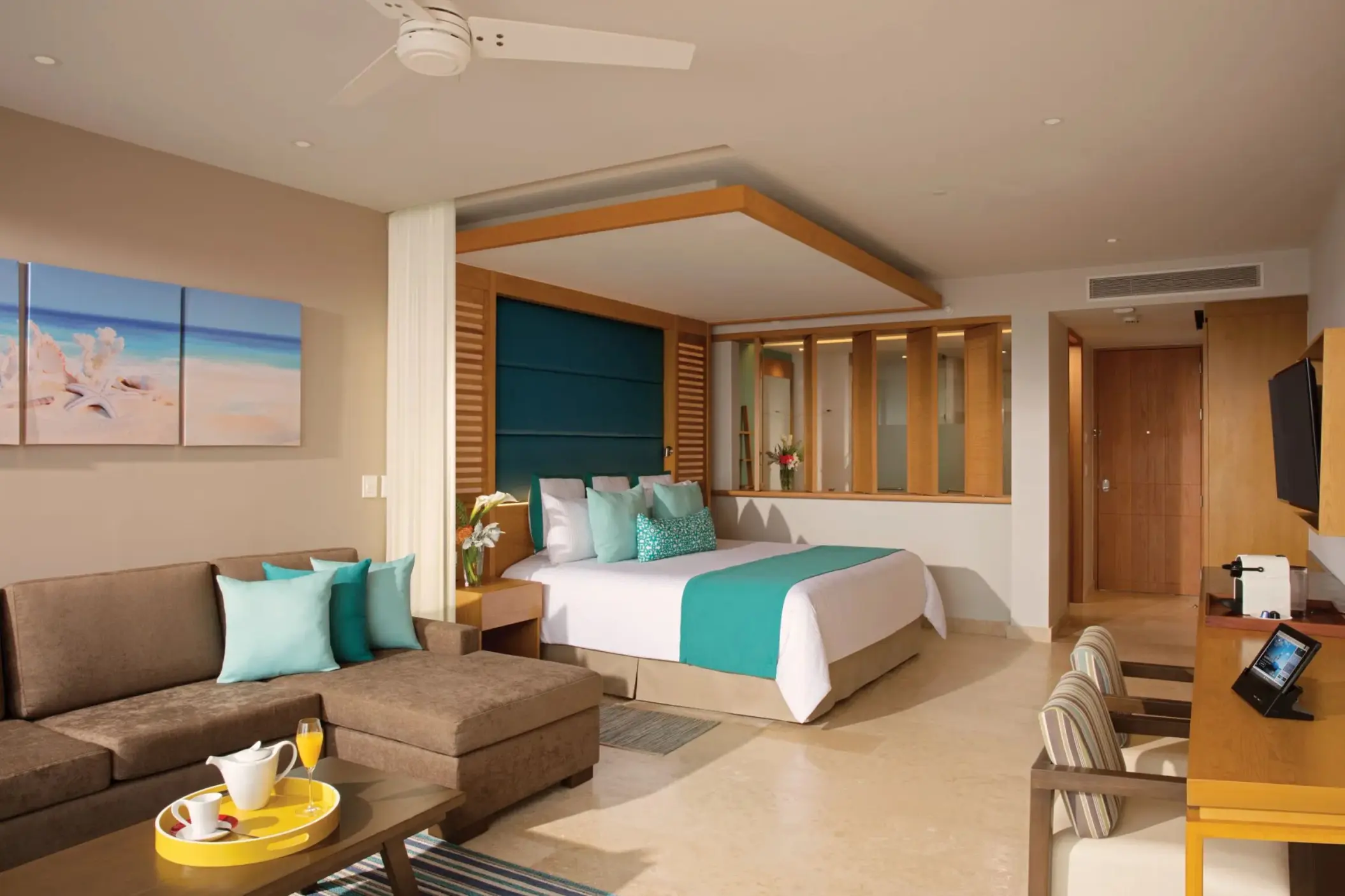Bright junior suite with teal accents, plush couch, dining space, and a cozy king-size bed.