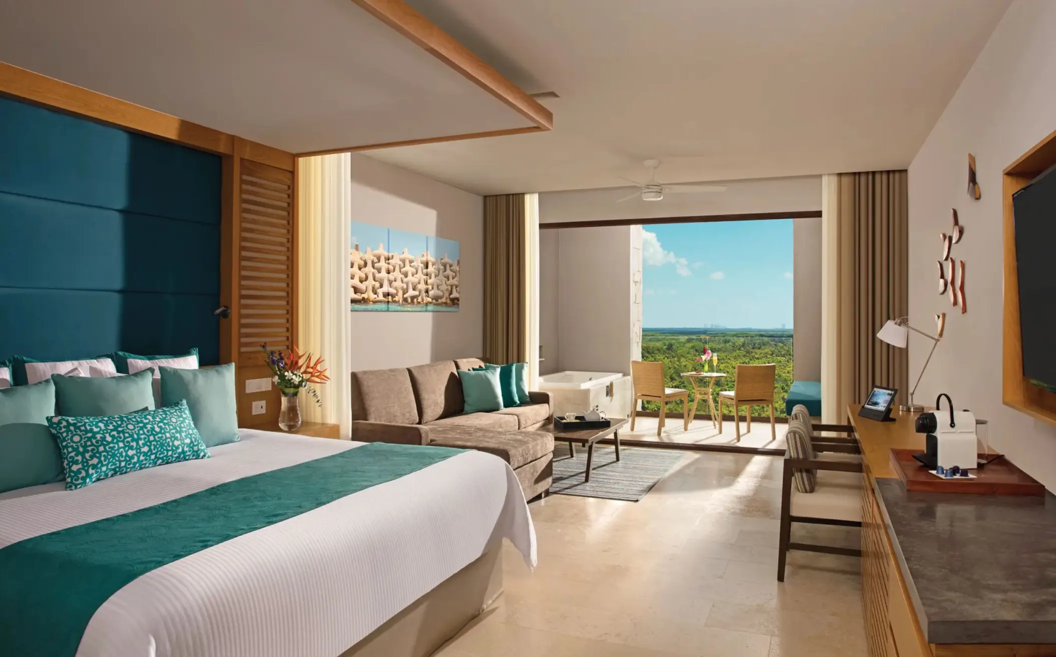 Spacious junior suite with king bed, sofa area, and balcony overlooking lush green tropical scenery.
