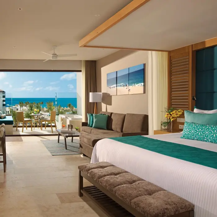 Junior suite with ocean view, king bed, cozy seating area, and furnished balcony at Dreams Resort.