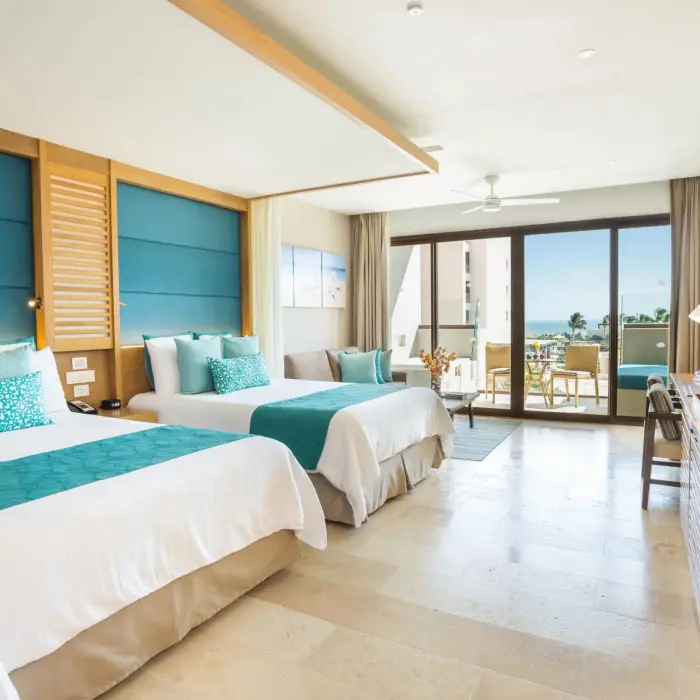 Bright junior suite with double beds, teal accents, and ocean view balcony at Dreams Playa Mujeres.