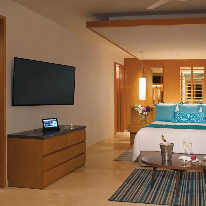 Stylish bedroom suite with teal accents, king bed, and view into spacious adjoining living area.