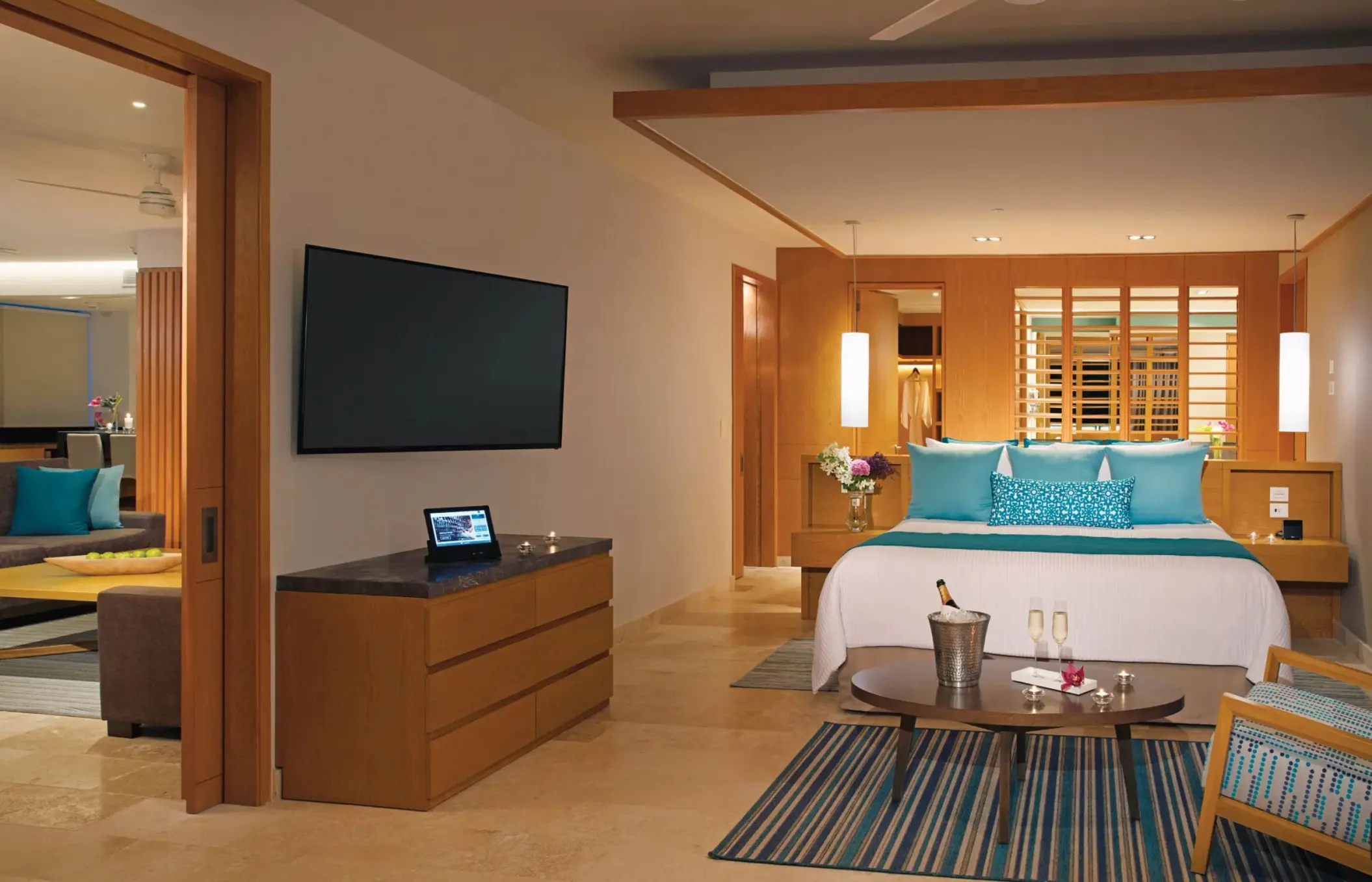Stylish bedroom suite with teal accents, king bed, and view into spacious adjoining living area.