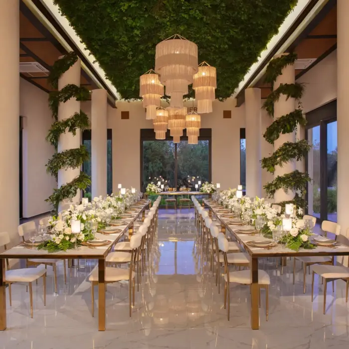 Elegant wedding reception setup in a bright ballroom with lush greenery, chandeliers, and mirrored tables.