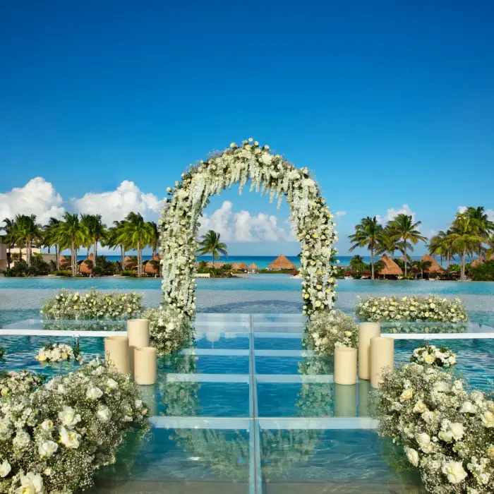 Scenic mermaid pool ceremony setup with floral arch, floating aisle, and ocean view backdrop.
