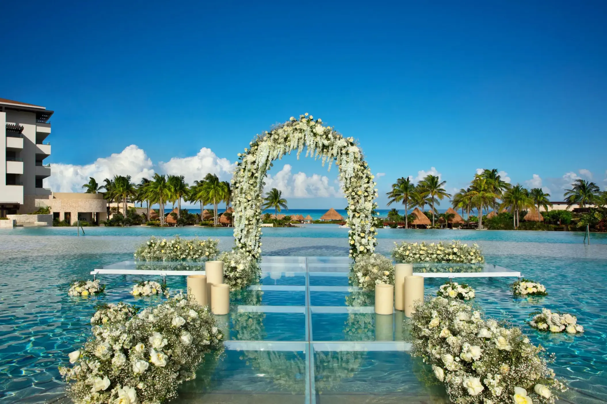 Scenic mermaid pool ceremony setup with floral arch, floating aisle, and ocean view backdrop.