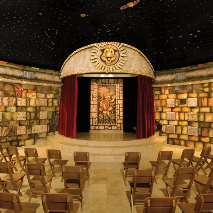 Explorer’s Club indoor kids’ theater with stage, red curtains, and Mayan-inspired décor.