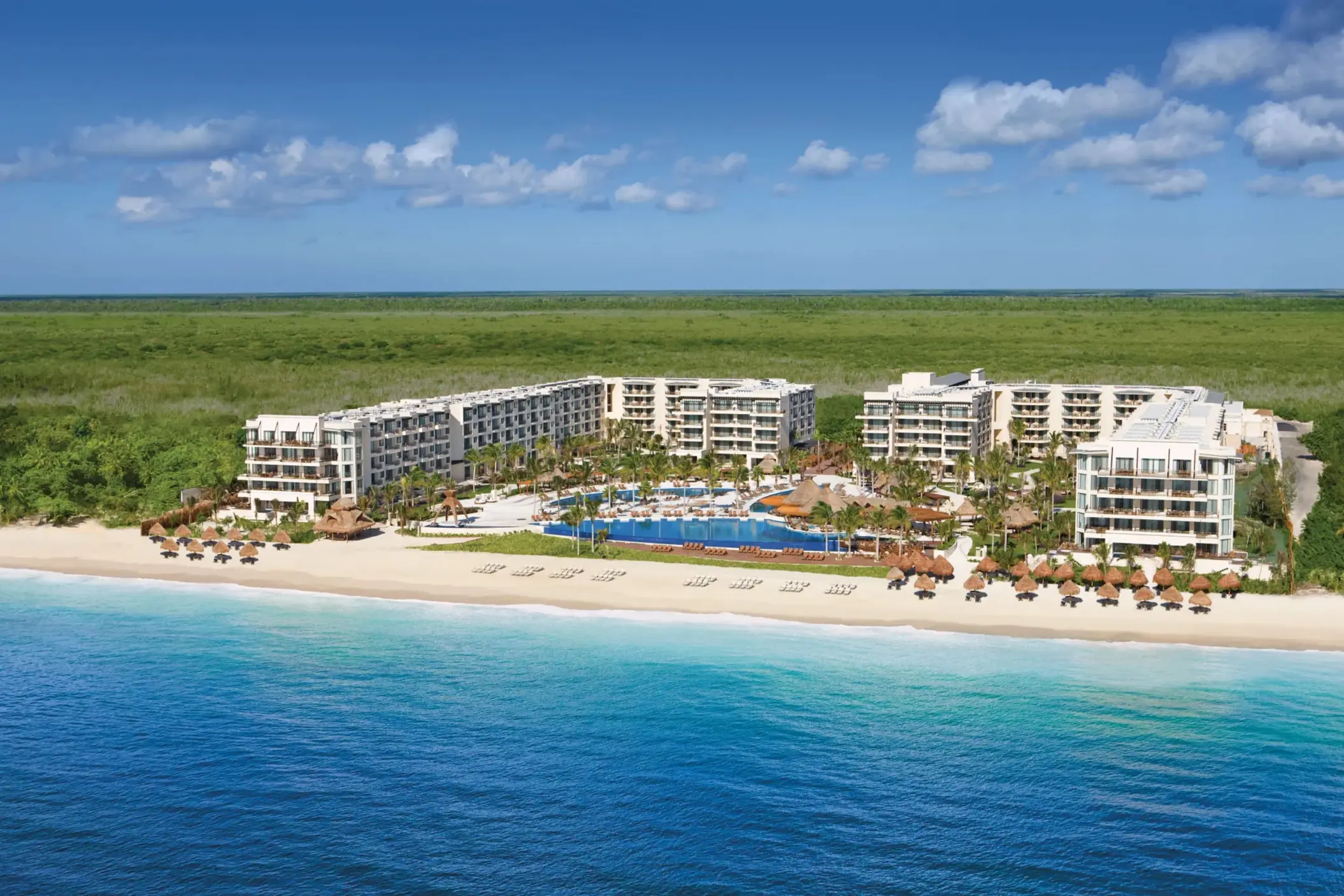 Aerial image of Dreams resort surrounded by forest, overlooking a white-sand beach.