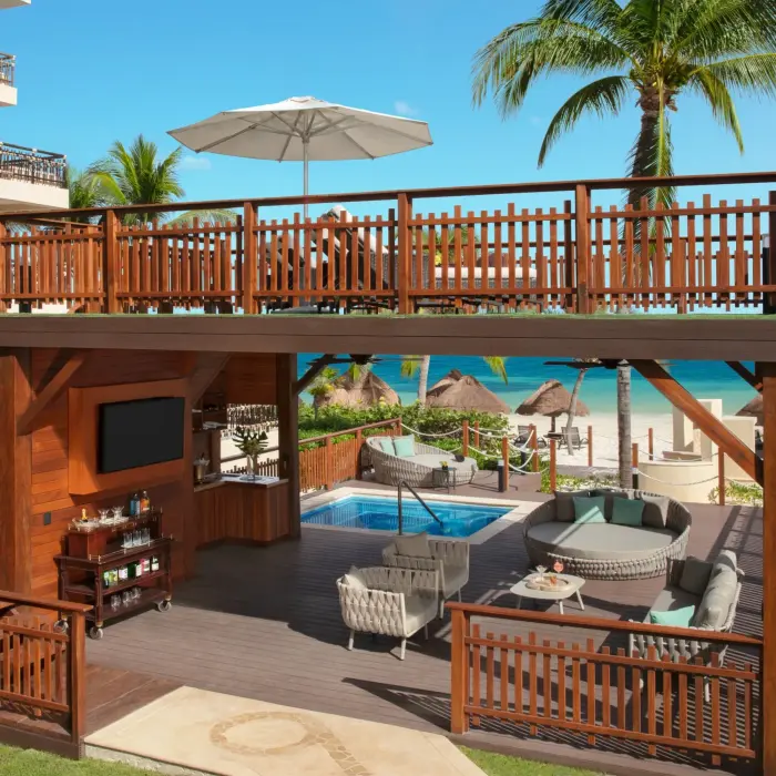 Outdoor beach cabana with lounge seating, sun deck and ocean backdrop.