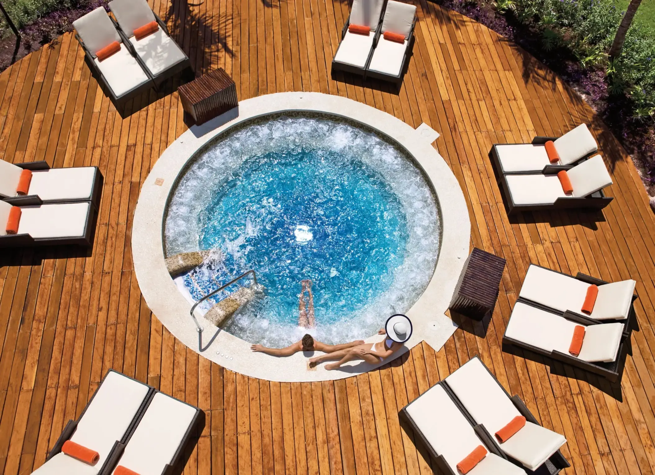 Circular outdoor whirlpool surrounded by sun loungers on a wooden deck.